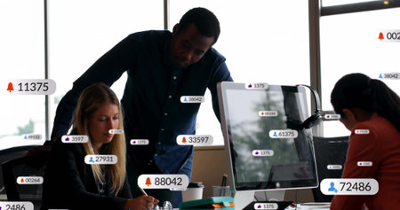 Collaborating three business colleagues reviewing data at office desk, with notebook, monitor....