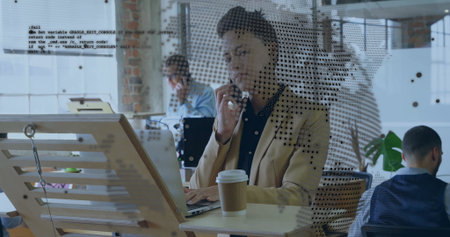 Talking Black woman typing on laptop while holding smartphone in open-plan office with coffee. Collaboration, teamwork, productivity, modern, professional, workspace, corporateの写真素材