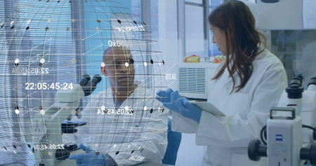 Discussing hologram data two scientists wearing white lab coats at lab bench, using tablet computer....