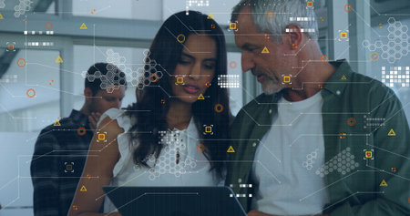 Collaborating colleagues wearing casual attire focusing on laptop at office with HUD overlays. Technology, innovation, teamwork, digital, modern, communication, enterpriseの写真素材