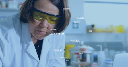 Scientist in lab coat and goggles inspecting beaker at lab bench, with laptop and digital overlays....
