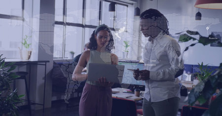 Collaborating coworkers analyzing data on laptop in open-plan office, with world map and smartphone. Collaboration, teamwork, modernoffice, dataanalysis, professionalenvironment, digitalworkspace, corporateの写真素材