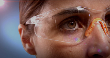 Adult woman inspecting safety glasses in lab, with orange nose pad reflecting colored flares....