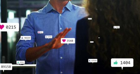 Gesturing businessman in light blue shirt speaking to colleague in office, with engagement icons....