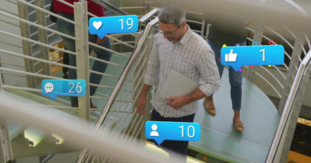 Walking staff in casual attire carrying laptop on metal staircase in atrium showing media overlays....