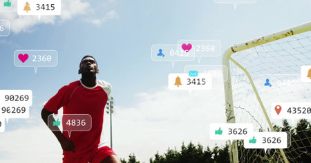 Standing soccer player in red uniform scanning sky beside goal, with social media icons copy space. Athlete, sports, outdoor, digital, engagement, vibrant, determinationの写真素材