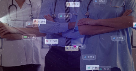 Standing team in medical attire crossing arms in clinic with stethoscopes and social media icons. Healthcare, professionalism, teamwork, digital engagement, medical staff, clinical environment, communicationの写真素材