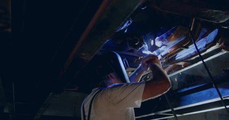 Welding technician wearing helmet welding overhead beams with torch at metal shop, sparks flying....