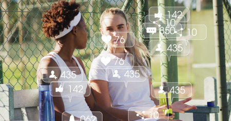 Sitting adult female tennis players chatting on bench beside fence. Activewear, sportsmanship, outdoorathletics, fitness, camaraderie, leisure, vibrantの写真素材