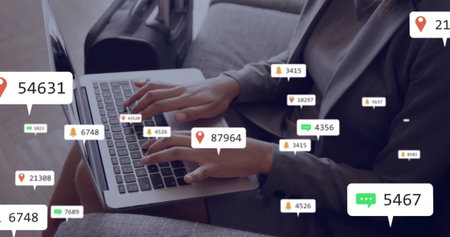 Businesswoman in blazer typing on laptop in airport lounge, with carry-on suitcase, notifications. Corporate, travel, professional, technology, connectivity, modern, urbanの写真素材