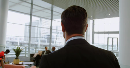 Standing Asian man wearing dark business suit reading folder in office lounge, with potted plant. Professional, corporate, modern, collaborative, executive, teamwork, interiorの写真素材