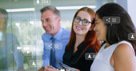 Three professionals reviewing social media icons on glass panel in office, with tablet and stylus. Modern, collaborative, analytical, innovative, digital, corporate, productiveの写真素材