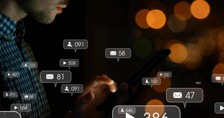 Tapping man in blue shirt checking notification overlays on smartphone in dark room, copy space....