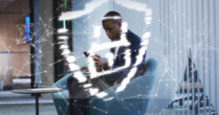 Tapping smartphone man wearing dark suit in blue chair in reception with network overlay. Professional, technology, business, innovation, connectivity, modern, corporateの写真素材
