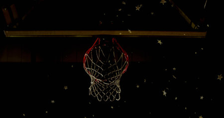 Shining basketball hoop with red rim and white net in dim court, with floating star decorations. Sports equipment, athletic, dynamic, minimalist, vibrant, performance, celestialの写真素材