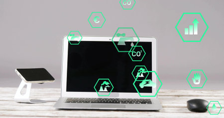 Silver laptop computer sitting on wood desk in office, with smartphone stand, mouse and green icons. Technology, sustainability, modern, workspace, digital, productivity, environmentの写真素材