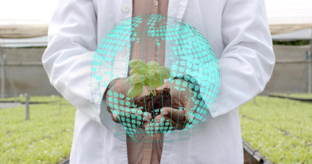 Presenting lab coat scientist holding green seedling with roots in greenhouse, with globe overlay....