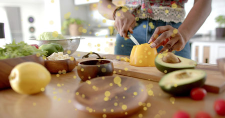 Home cook slicing yellow pepper on wooden cutting board in home kitchen, with avocado and tomatoes....