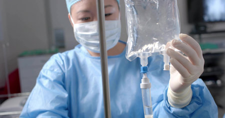 Korean medical professional in surgical attire adjusting IV fluid and tubing on IV pole in clinic....