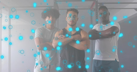 Partners posing with arms crossed in weight room, with squat rack, weight plates, hexagon overlay. Fitness, strength, technology, camaraderie, athleticism, innovation, workoutの写真素材