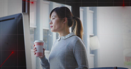 Office woman holding paper coffee cup and gazing out city window in modern office, computer monitor. Professional, contemporary, minimalism, productivity, urban, daylight, workspaceの写真素材