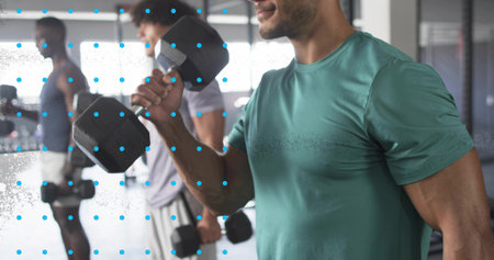 Performing bicep curls, man in teal T-shirt using hexagonal dumbbell in gym weight area, copy space. Fitness, strength, training, health, activewear, gym, wellnessの写真素材