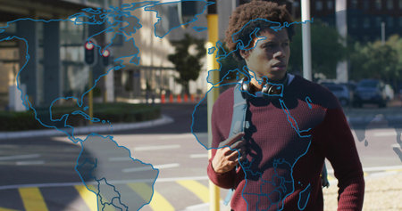 Man wearing sweater and headphones waiting at traffic light crosswalk, with world map overlay....