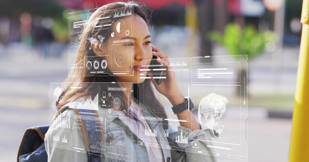 Woman accessing holographic data while talking on smartphone at city sidewalk, wearing denim jacket. Technology, urban, innovation, business, communication, futuristic, streetの写真素材