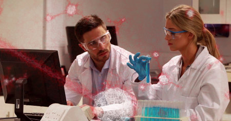 Researchers wearing safety gear examining blue liquid test tube at lab bench, with test tube rack....