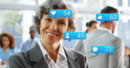 Smiling senior businesswoman wearing gray blazer, striped shirt in office with social media icons....