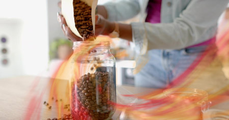 Woman in denim jacket pouring coffee beans from paper bag into glass jar on kitchen countertop. Rustic, cozy, minimalism, culinary, lifestyle, preparation, domesticの写真素材