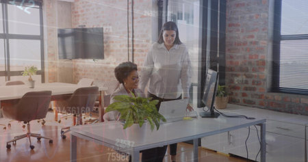Two coworkers wearing business attire reviewing laptop content in open office with potted plant. Collaboration, teamwork, modern, professional, workspace, interior, innovationの写真素材
