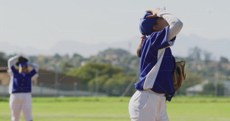 Adjusting baseball player wearing cap holding glove on field with chainlink fence, copy space. Athletic, teamwork, outdoor, sport, competition, leisure, fitnessの写真素材