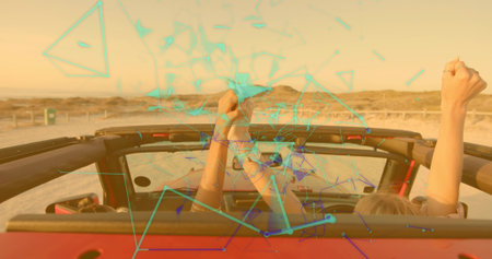 Driving two friends raising arms atop red convertible on coastal highway by rope fence golden hour....