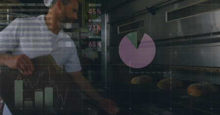 Baker in white shirt placing loaves onto oven racks in bakery, with digital charts, copy space....