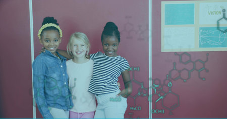 Standing three student girls smiling in science classroom, with Vision poster and chemical diagrams....