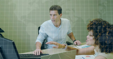 Two office professionals analyzing data at office desk, with desktop monitor and printed charts....