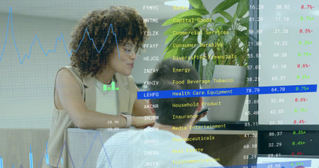 Stock analyst wearing vest reviewing data on laptop and smartphone in office lounge, with overlays....