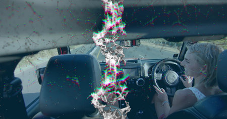 Steering woman holding smartphone in right-drive car on rural road, with mirror, copy space. Digital...