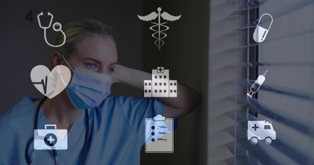 Leaning worker in scrubs mask stethoscope gazing through blinds in clinic overlaid medical icons. Medical, healthcare, hospital, clinical, professionalism, safety, diagnosticsの写真素材