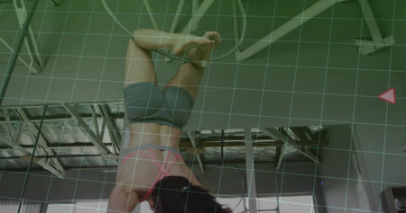 Hanging aerialist executing inverted pose in fitness studio, with hoop rigging and grid overlay. Acrobatics, flexibility, athleticism, modern, industrial, choreography, motionの写真素材