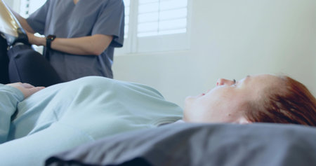 Recording nurse checking patient lying on examination bed in exam room, with tablet and smartwatch....