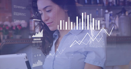 Holding white tablet, woman in blue shirt viewing digital charts at coffee counter, copy space. Technology, productivity, contemporary, workspace, innovation, communication, lifestyleの写真素材