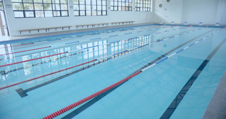 Empty lap pool occupying central pool hall, with red and blue lane dividers and wooden bench....