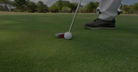 Lining up golfer in golf shoes placing putter behind white golf ball on putting green. Athletic, outdoor, landscape, precision, competition, sport, leisureの写真素材
