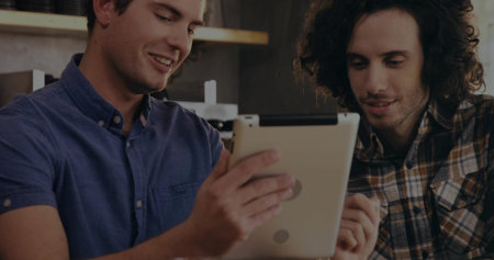 Two adult men collaborating over tablet at coffee shop metal countertop, with espresso machine. Collaboration, teamwork, networking, professional, casual, modern, interiorの写真素材