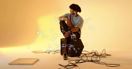 Sitting man wearing t-shirt, earphones on black amplifier at studio, surrounded by audio cables. Musician, recording, production, minimalism, modern, creativity, soundの写真素材