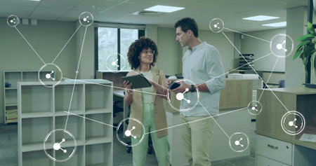 Discussing data sharing in modern open-plan office, with tablet and network icons. Collaboration,...