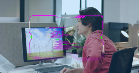 Focusing man wearing red shirt coding on desktop monitor at office desk, with keyboard headphones. Technological, productivity, innovative, professional, contemporary, analytic, startupの写真素材