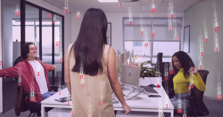 Standing professional wearing dress engaging with colleagues at office desk, with binary overlay....